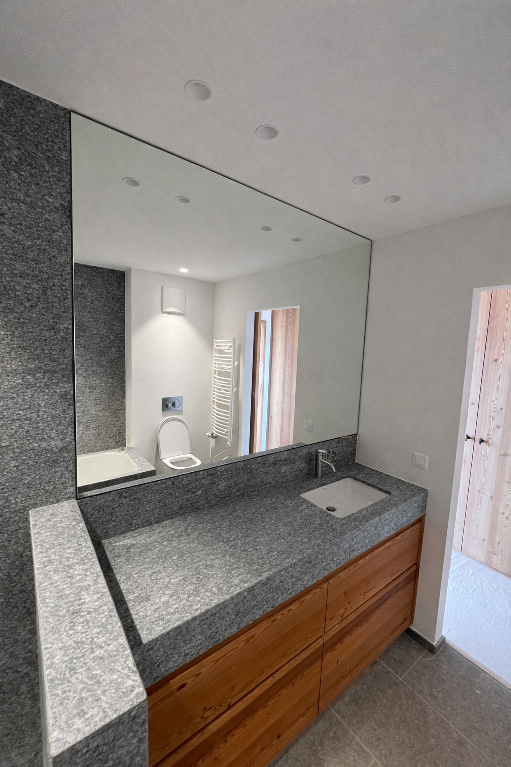 Miroir mural sur mesure en salle de bain moderne avec meuble en bois et plan vasque en pierre naturelle.