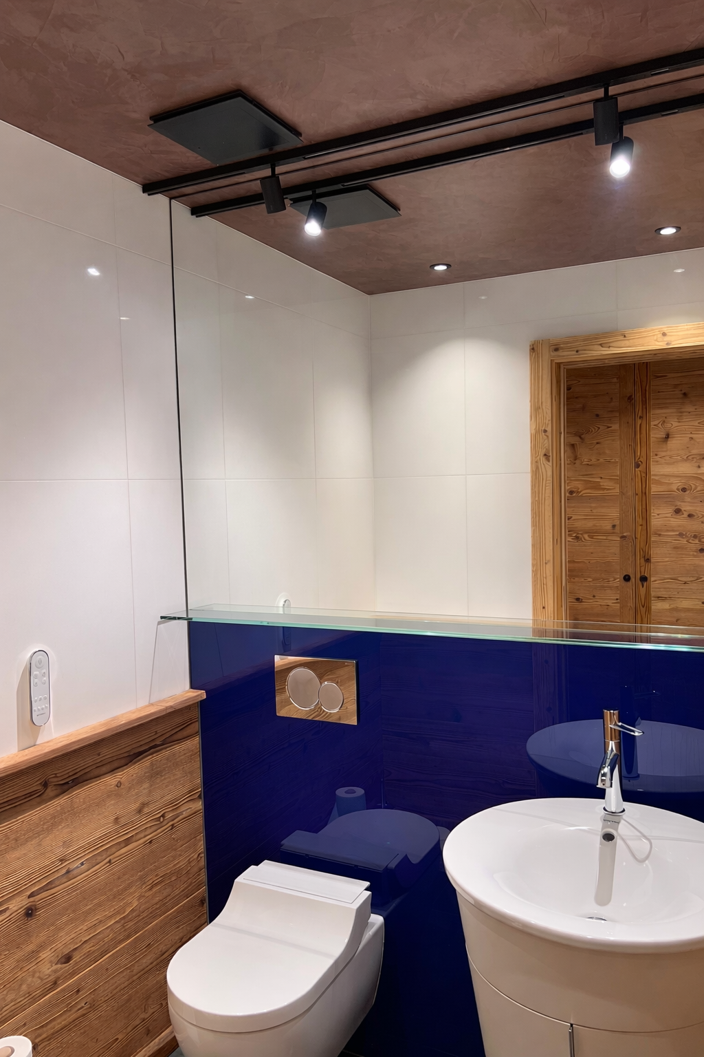 Paroi en verre teinté bleu pour WC design avec finition bois et éclairage intégré – réalisation miroiterie sur mesure.