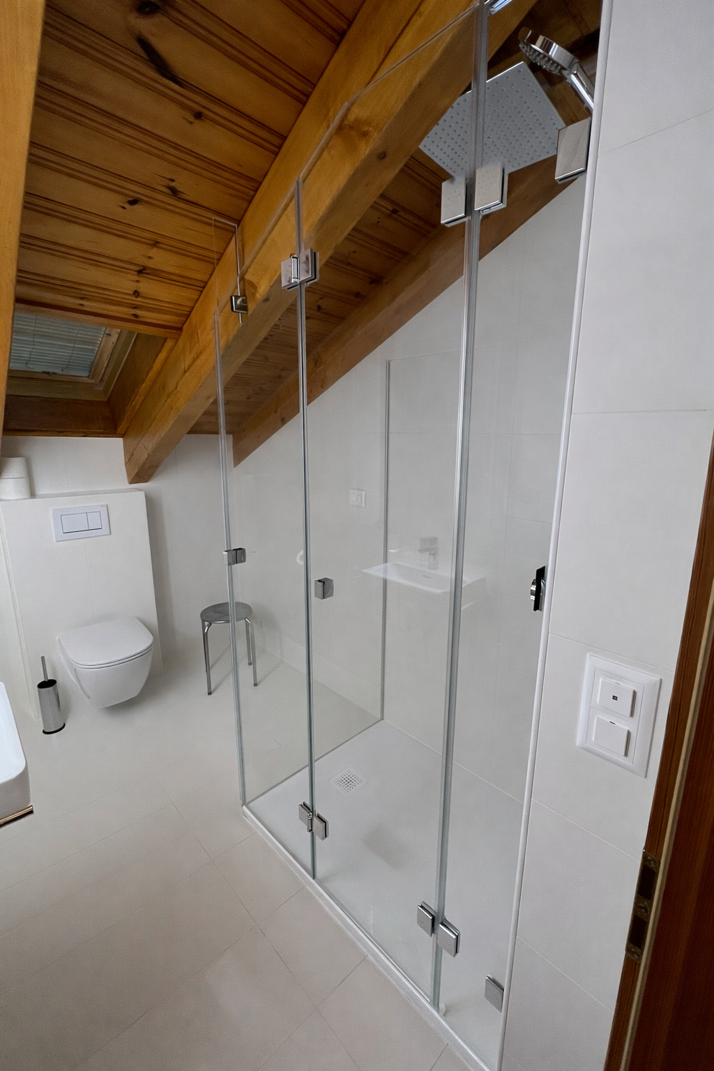 Cabine de douche en verre sécurit sur mesure sous toiture avec poutres en bois.